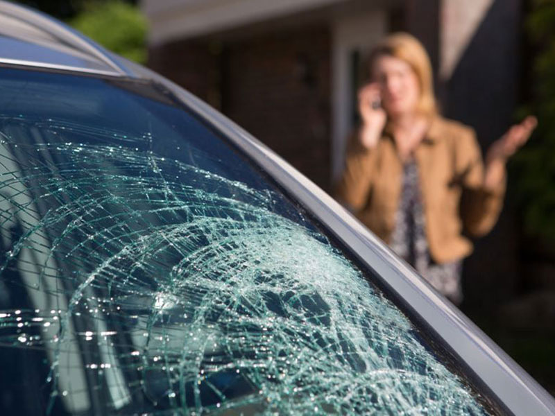 Broken Windshield of a car and a woman talking on the phone in the background